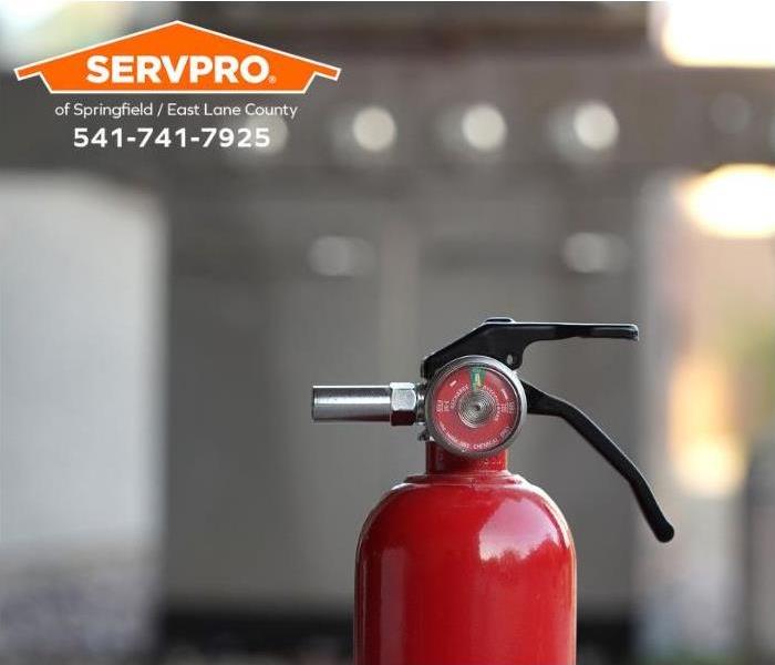 A close-up of a fire extinguisher is shown sitting in front of an outdoor barbeque.