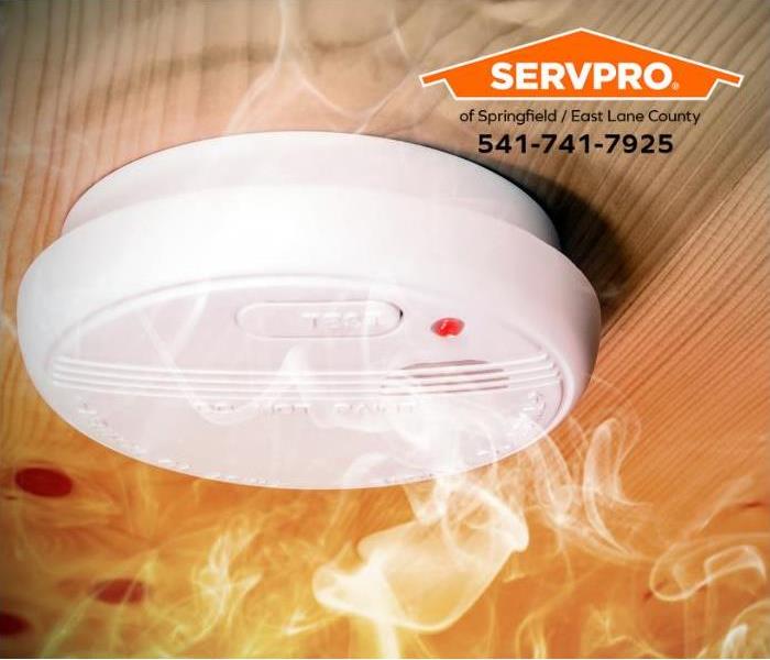 Smoke rises towards a smoke detector mounted on a ceiling.